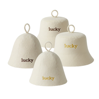 Four cream-colored felt bell-shaped sauna hats with hanging loops, each embroidered with the word 'lucky' in different font colors: two in dark brown, two in gold.