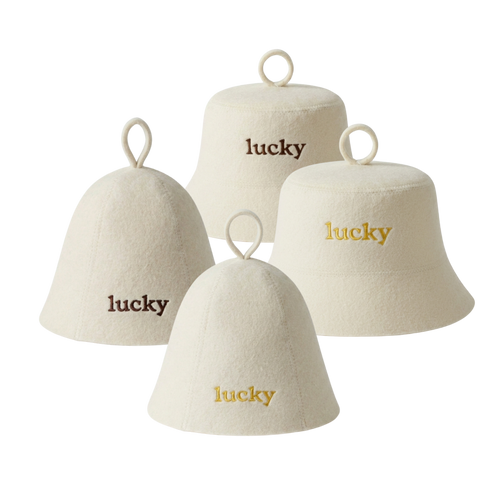 Four cream-colored felt bell-shaped sauna hats with hanging loops, each embroidered with the word 'lucky' in different font colors: two in dark brown, two in gold.